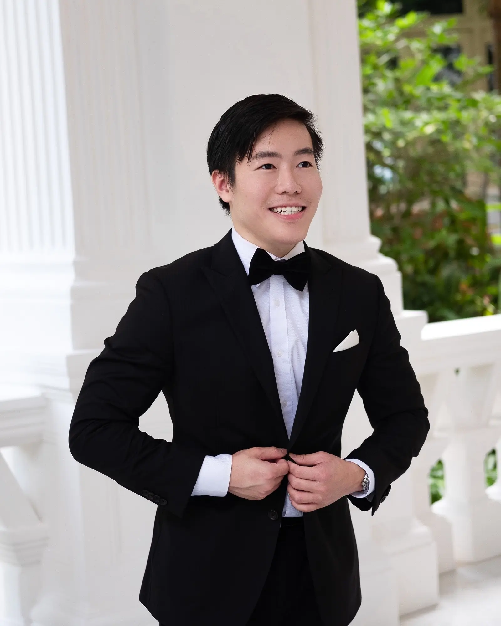 Luke Lee in black tie on a white colonnaded verandah